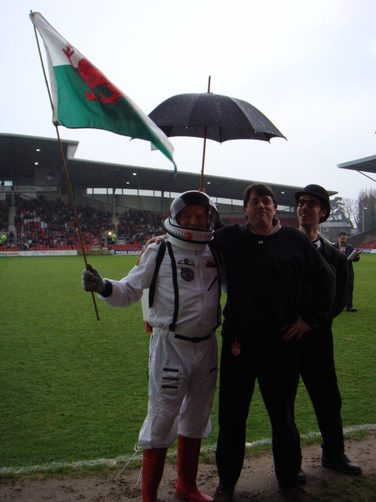 An astronaut, his bowler hatted assistant and a lunatic in the rain on the edge of the pitch prior to the game.