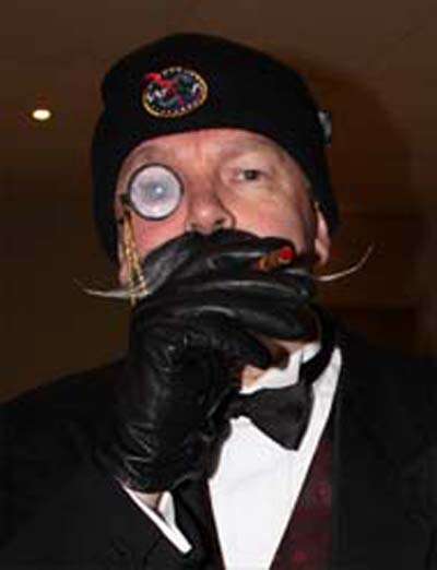 Monocled man in tuxedo and bow tie wearing a WASA hat smoking a cigar