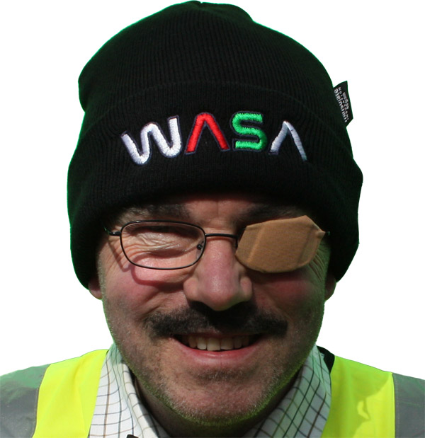 A man wearing a hi-viz vest wearing a woolly hat with the letters WASA on it. He has a sticking plaster patch over his left eye.