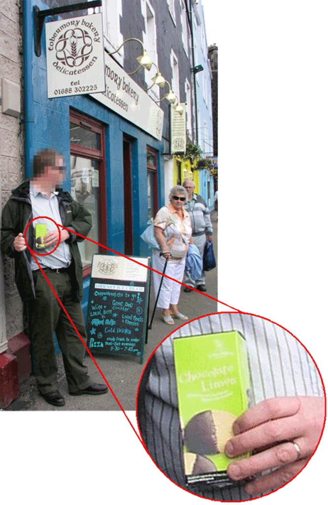 A man appears to be concealing a packet of biscuits under his coat as an elderly lady looks on outside a shop in Tobermory