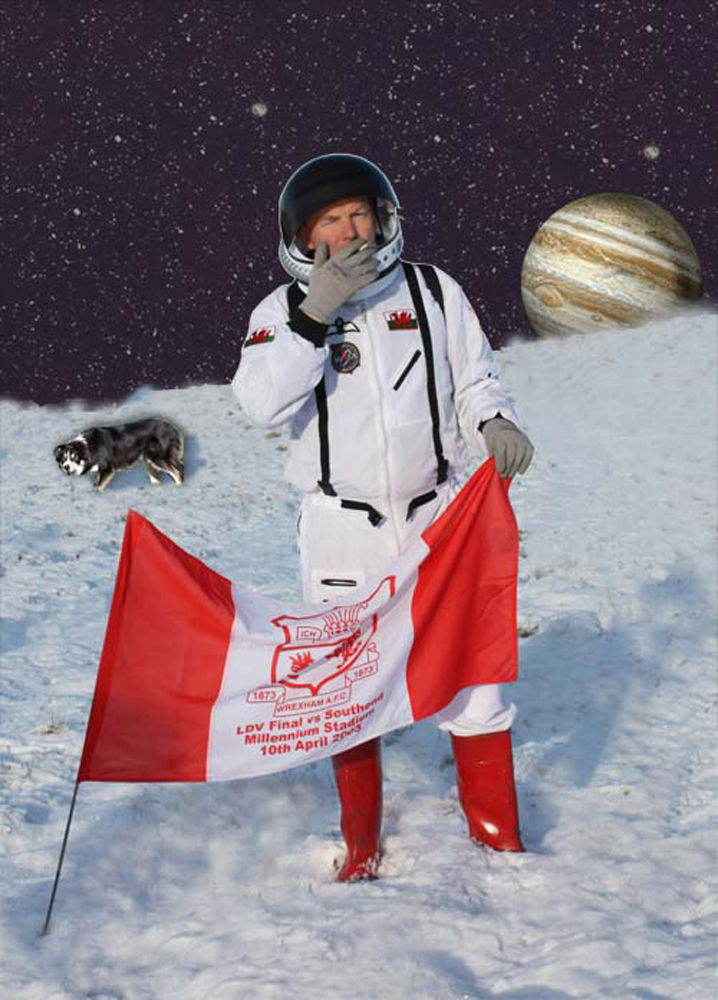 A spaceman on the surface of Europa smoking a cigarette whilst holding a Wrexham FC flag. Behind him is a sheepdog, and over the horizon is Jupiter