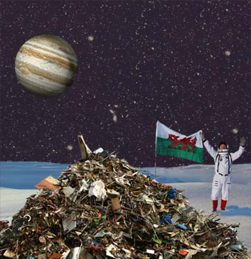 A pile of rubbish on a frozen lunar landscape with a man in a spacesuit holding aloft a Cymru flag.  Jupiter visible over the horizon
