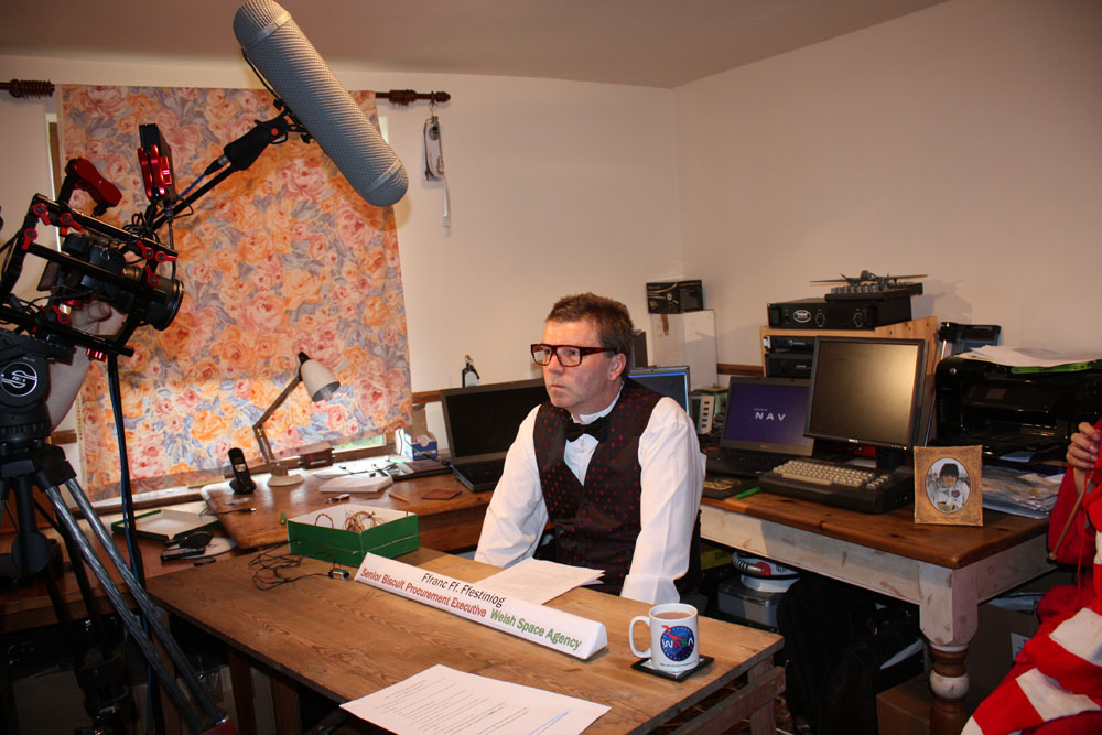 Welsh Space Agency's Biscuit Procurement Executive Ffranc Ff Ffestiniog gives an interview to camera from his desk.