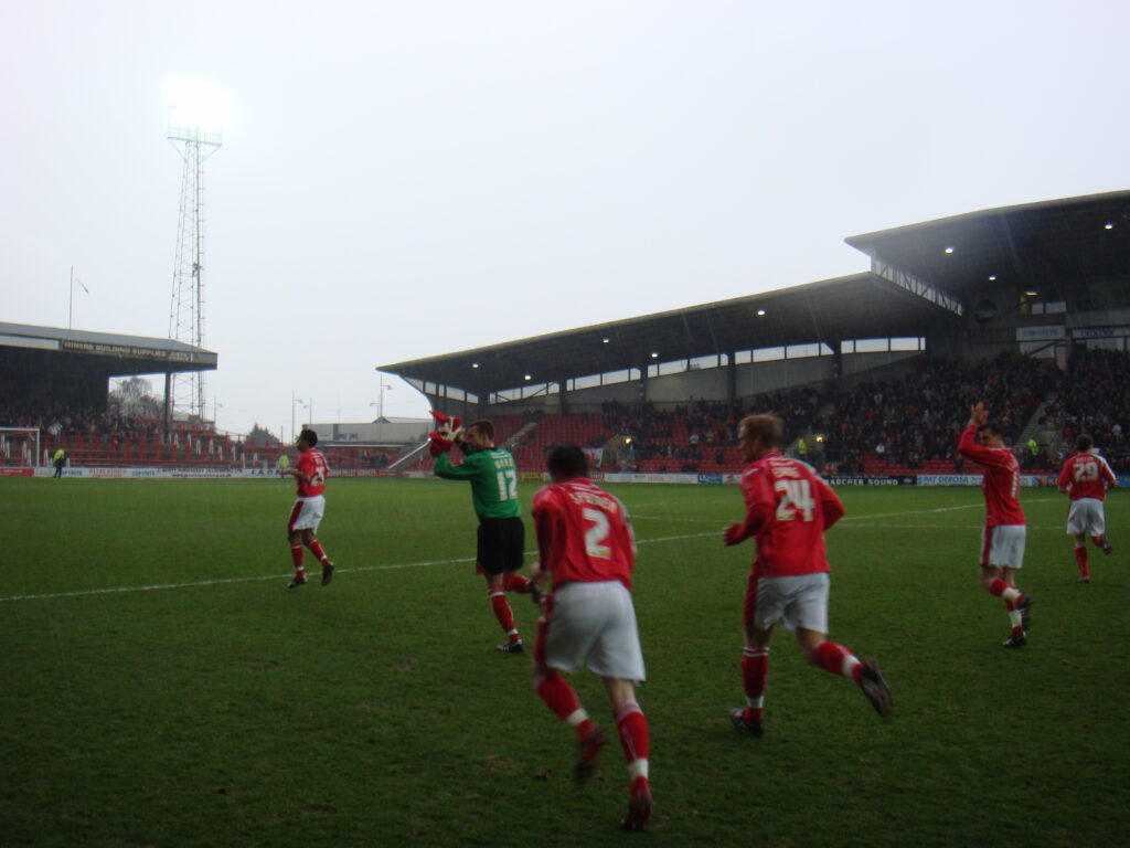 Footballer players of Wrexham run out on to the pitch on a rainy day.